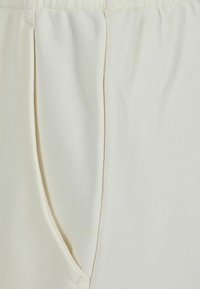 Nahaufnahme der seitlichen Tasche und Naht an cremefarbenen Strickhosen mit gerafftem elastischen Bund.