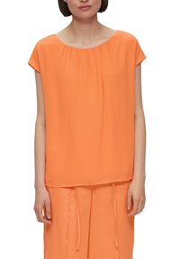Blusa arancione a maniche corte con scollatura rotonda e morbidi plissè. Tessuto leggero, vestibilità rilassata, abbinata a pantaloni larghi arancioni coordinate.