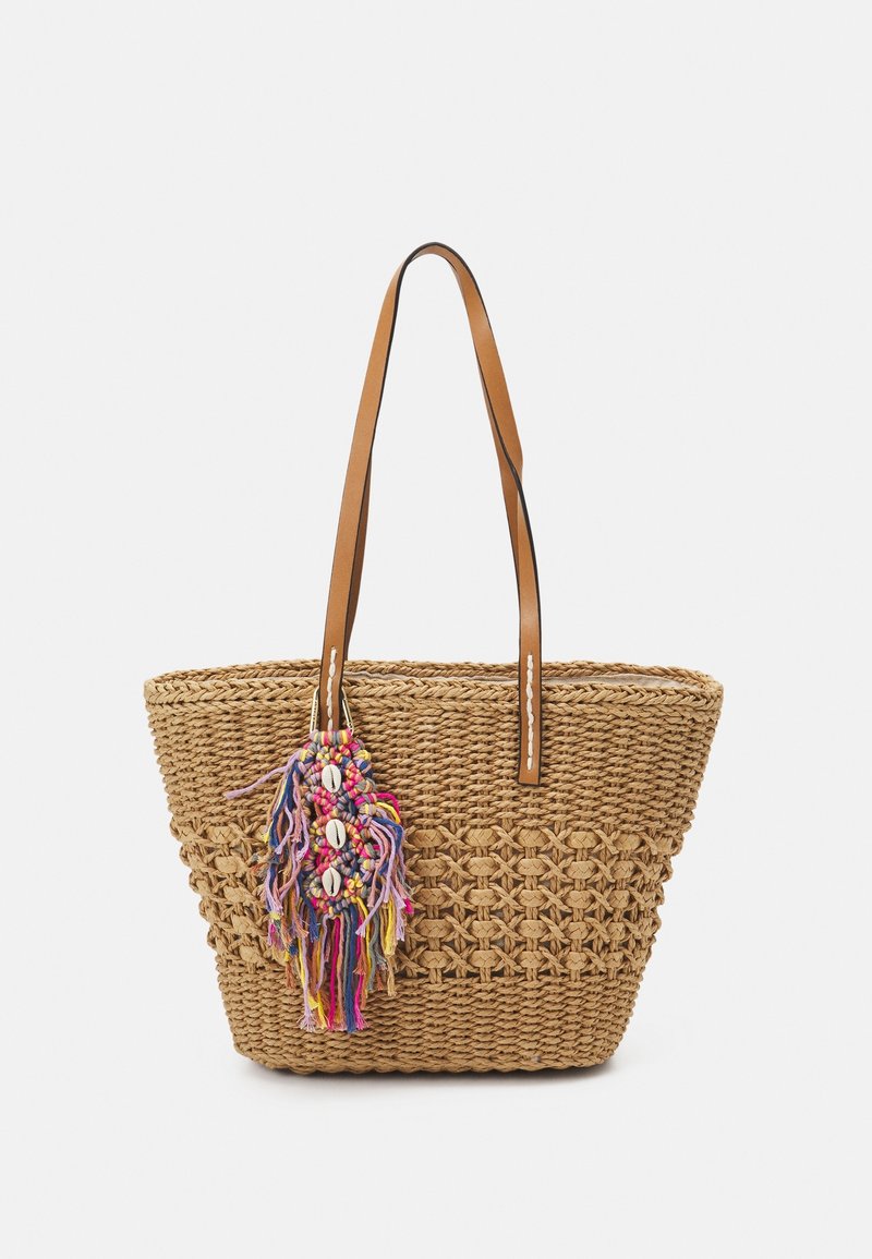 Sac fourre-tout en paille tissée avec deux poignées en cuir marron et un pompon coloré en fil décoré de coquillages blancs suspendu à l'avant.