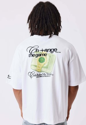 Personne avec des dreadlocks portant un t-shirt blanc affichant un graphique montre et argent liquide avec le texte "Change the game" et "Cash Rules My Time."