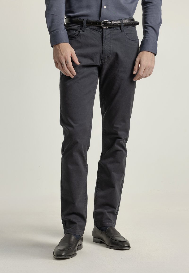 Pantalones de algodón azul marino con corte ajustado, cinco bolsillos y trabillas para cinturón, combinados con zapatos de cuero negro y un cinturón a juego.