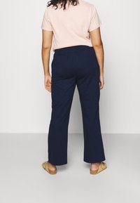 Pantaloni larghi blu navy con cintura elastica, tessuto strutturato, indossati con una maglietta rosa chiaro e scarpe flat beige.
