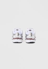 Λευκά αθλητικά παπούτσια με μεταλλικές ασημί λεπτομέρειες, επάνω μέρος από υφασμένο δίχτυ με υφή, επενδεδυμένος γιακάς και μαύρη λαστιχένια εξωτερική σόλα. Πίσω όψη που αναδεικνύει τα χαρακτηριστικά σχεδίασης.