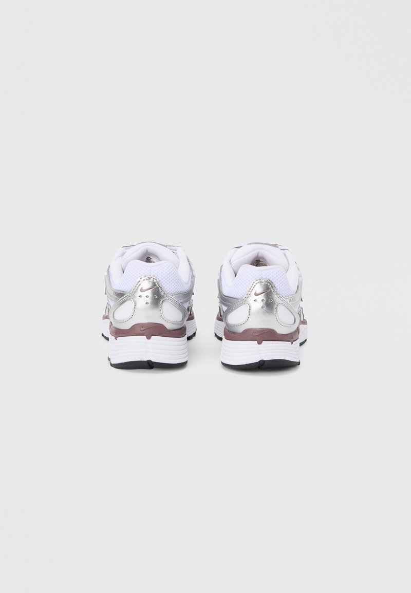Chaussures de sport blanches avec accents argentés métalliques, dessus en mesh texturé, col rembourré et semelle extérieure en caoutchouc noir. Vue arrière mettant en évidence les caractéristiques de design.