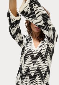 Pullover lavorato a maglia con un motivo a zigzag bianco e nero, scollatura a V e tessuto testurizzato con maniche lunghe.