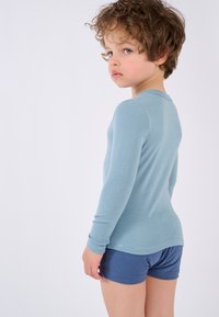 Maglietta a maniche lunghe di colore azzurro chiaro e pantaloni corti blu. La maglietta ha una texture a coste e un colletto rotondo, mentre i pantaloni corti presentano una cintura elastica.