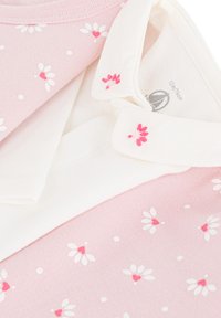 Outfit per neonati rosa con motivo floreale bianco e colletto bianco decorato con piccoli fiori ricamati rosa, piegato su uno sfondo bianco.