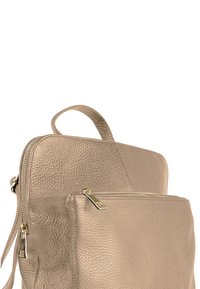 Beige leren rugzak met textuur, een bovenhandgreep en een voorvak met rits. Voorzien van gouden hardware accenten en een minimalistisch design.