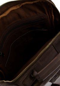 Interieur van een bruine leren tas met een stoffen voering in twee kleuren. Bevat een ritsvak en een plat compartiment voor organisatie.