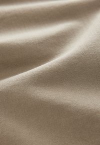 Beige stof met een zachte, gestructureerde weving en een subtiele glans. Het materiaal oogt glad met zachte plooien en een consistent patroon.