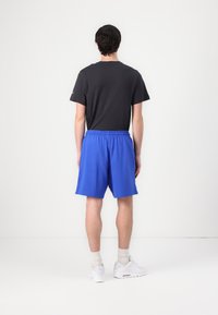 Camiseta preta de manga curta e calções azuis com cintura elástica, ténis brancos, fundo branco liso.