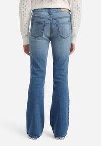 Jeans in denim blu a zampa d'elefante con un lavaggio chiaro, dotati di tasche posteriori, dettagli di cucitura sottili e vita a media altezza.