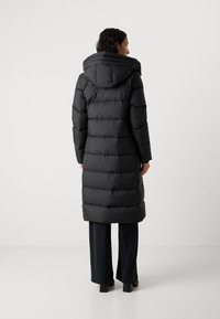 Zwarte pufferjas met een capuchon, voorzien van een gewatteerd ontwerp en een verlengde silhoët. Het materiaal lijkt glad en glanzend, wat de warmte benadrukt.