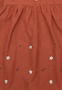 Rust-colored fabric dress featuring white floral embroidery and small brown leaves, with a gathered waist and button detail at the neckline.