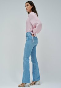 Blusa rosa clara con mangas abullonadas, atadas en la muñeca, combinada con jeans acampanados azul claro y sandalias de tacón beige.