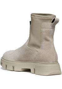 Des bottes chelsea beiges présentent un cuir lisse sur le dessus, un dos en suède texturé, une semelle épaisse rainurée et des détails de couture.