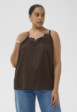 Femme portant un haut sans manches marron foncé orné de dentelle et un jean bleu, regardant sur le côté avec la main près de son épaule.