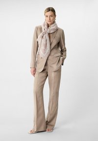 Beżowy dopasowany garnitur z przylegającą marynarką, szerokimi spodniami i jasnoróżowym, wzorzystym szalikiem. Gładki materiał o zorganizowanej konstrukcji.