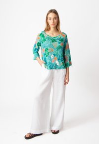 Top con stampa floreale con fiori verdi, blu e arancioni; vestibilità comoda. Abbinato a pantaloni in lino bianchi a gamba larga e sandali neri con cinturini.