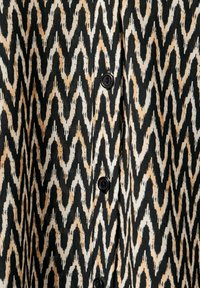 Tela de patrón zigzagueante en negro y beige con una textura suave y botones, que presenta un diseño geométrico audaz y una combinación de colores contrastante.