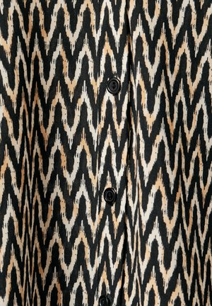 Czarny i beżowy materiał w zygzakowy wzór o gładkiej fakturze i guzikach, przedstawiający odważny geometryczny design oraz kontrastowy schemat kolorów.