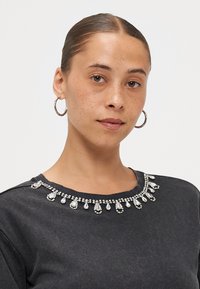 Grijze sweatshirt met een ronde hals, versierd met heldere rhinestones en druppelvormige accenten langs de halslijn. Soepele textuur.