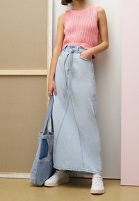 Jupe maxi en denim bleu clair avec des fentes latérales, assortie à un haut rose tricoté sans manches. Des baskets blanches et un sac fourre-tout bleu complètent la tenue.