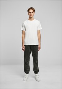 Hvid bomulds t-shirt og mørkegrå velour joggingbukser med elastiske manchetter. Skoene er hvide med en kraftig sål, placeret mod en neutral baggrund.