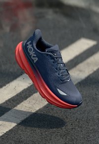 Chaussure avec une tige en maille navy respirante, semelle néon rose et logo proéminent. Comprend un design texturé et des accents réfléchissants. Construction légère.
