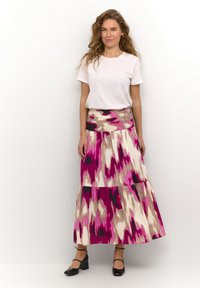 Gonna maxi con un design a strati nei colori rosa, beige e nero; vita testurizzata. Abbinata a una maglietta bianca e scarpe nere.