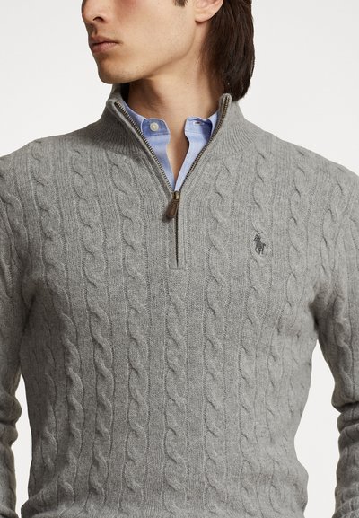 Gray cable-knit sweater with a zippered collar and a small logo on the chest. Layered over a light blue collared shirt.