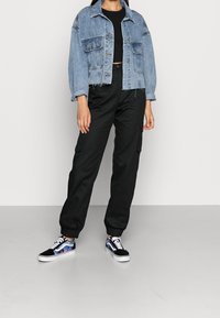 Obcisła, niebieska kurtka dżinsowa z dwiema kieszeniami na piersiach, noszona na czarnym topie; czarne spodnie cargo z elastycznymi mankietami; czarno-niebieskie trampki.