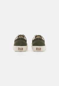 Zapatillas de ante verde con un diseño de cordones en beige, suela de goma blanca y un parche de logo prominente en el talón.