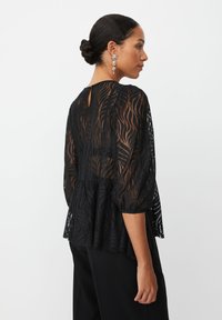 Sort gennemsigtig top med et bølgemønster, trekvartærmer og en nøglehul-rygdetalje. Flared peplum silhuet og tekstureret stof.