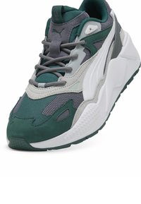 Sneakers verde închis și gri, realizate din plasă și nubuc, cu o talpă albă groasă, având tăieturi unice și detalii texturate pe partea superioară.