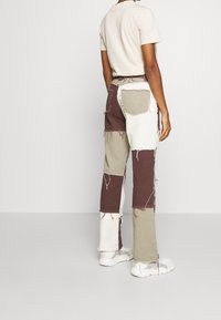 Lapppants i brunt, beige och vitt med fransade kanter, kombinerat med en ljus t-shirt och vita sneakers.