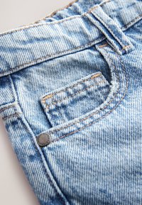 Hellblaue Jeans aus Denim mit strukturierter Oberfläche, ausgestattet mit einer kleinen Fronttasche und kontrastierenden Nähten, die durch einen Metallknopf gesichert sind.