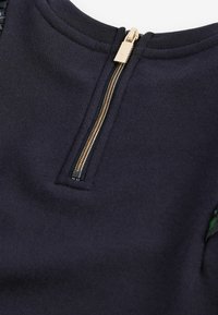 Granatowy sweatshirt z teksturowanej tkaniny, z złotym zamkiem z tyłu i zielonymi akcentami po bokach.