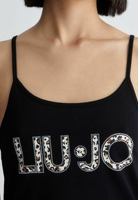 Czarny top na ramiączkach z cienkimi paskami, z tekstem "LIU:JO" napisanym dużymi literami. Litery mają wzór w panterę oraz akcenty z kryształków.