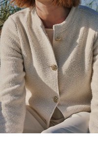 Cardigan in maglia color crema, con motivo strutturato, scollo rotondo e tre bottoni decorativi dorati sul davanti.