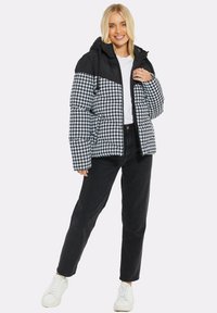 Sort og hvid hættepufferjakke med houndstooth mønster, lynlåslukning og elastiske manchetter, parret med sorte jeans og hvide sneakers.