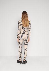 Beige bodysuit med svarte geometriske mønstre, lange ermer og tettsittende leggings-stil. Brukt med svarte sko med chunky såle.