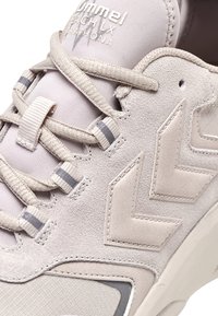 Ljusgrå sneakers med en kombination av mocka och meshmaterial. Accenterade med grå ränder och en geometrisk logotyp på sidan.