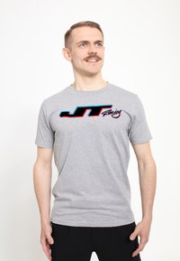 Šedé bavlněné tričko s krátkými rukávy, které má černé, modré a červené logo "JT Racing" na hrudi. Jednoduchý, uvolněný střih.