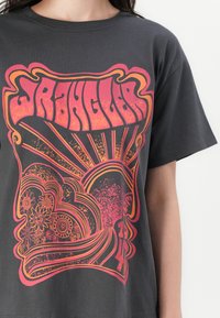 Schwarzes Baumwoll-T-Shirt mit einem lebhaften, psychedelischen Grafikdesign in Rot und Orange, das florale und sonnenstrahlenartige Motive zeigt. Lockere Passform.