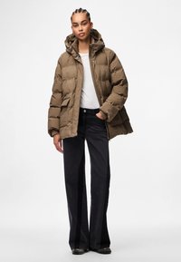 Chaqueta acolchada marrón con capucha, con cierre frontal de cremallera, dos bolsillos laterales y puños elásticos, combinada con pantalones negros de pierna ancha.