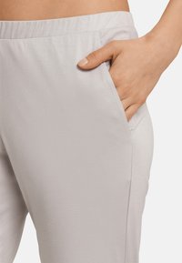 Lichtgrijze joggers van zacht materiaal, met een zijzak en een losse pasvorm, en een elastische tailleband voor comfort.