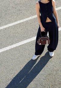 Námořnicky modrý top bez rukávů s knoflíky, široké kalhoty, bílé tenisky a malá hnědá kabelka s bílými pruhy a zaoblenými rukojetí.