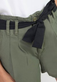 Shorts verts en tissu léger avec une ceinture en tissu noir nouée à la taille. Comprend des passants de ceinture et deux poches latérales.