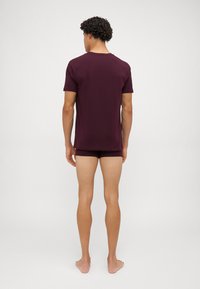 Burgundowa koszulka z krótkim rękawem i dopasowane szorty. Miękki materiał, luźny krój, okrągły dekolt i minimalistyczny design. Gładka tekstura.